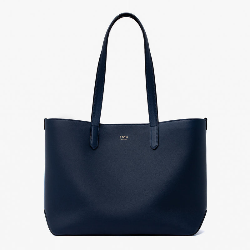 Stow London's Everyday Tote Bag in Navy smooth leather on a light grey background featuring gold STOW logo