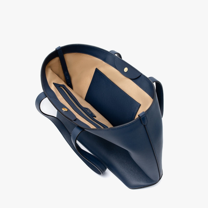 Stow London's Everyday Tote Bag in Navy smooth leather on a light grey background with magnets open showing the interior slip and zip pockets 