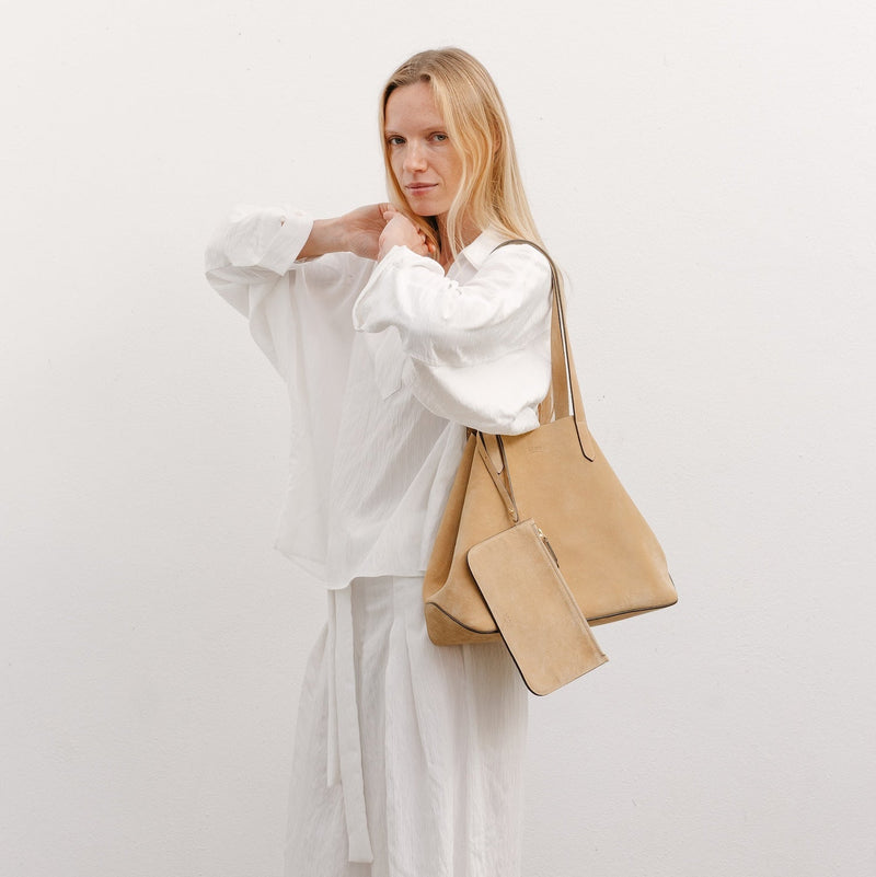 Model wearing STOW London's Everyday Tote bag in Soft Sand suede featuring its matching suede interior pouch and a small STOW London logo embossed on the front panel 