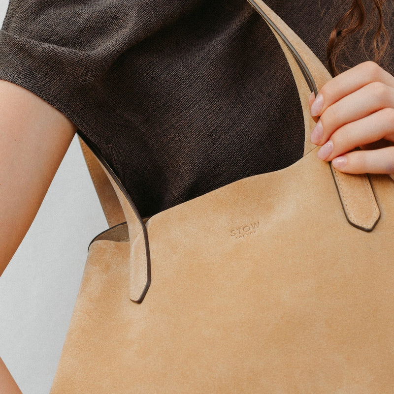 Close up of model holding STOW London's summer Everyday Tote in Soft Sand Suede, featuring a small embossed STOW London on the front panel 
