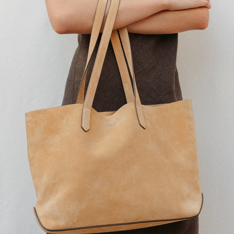 Model holding STOW London's summer Everyday Tote in Soft Sand Suede, featuring a small embossed STOW London on the front panel 