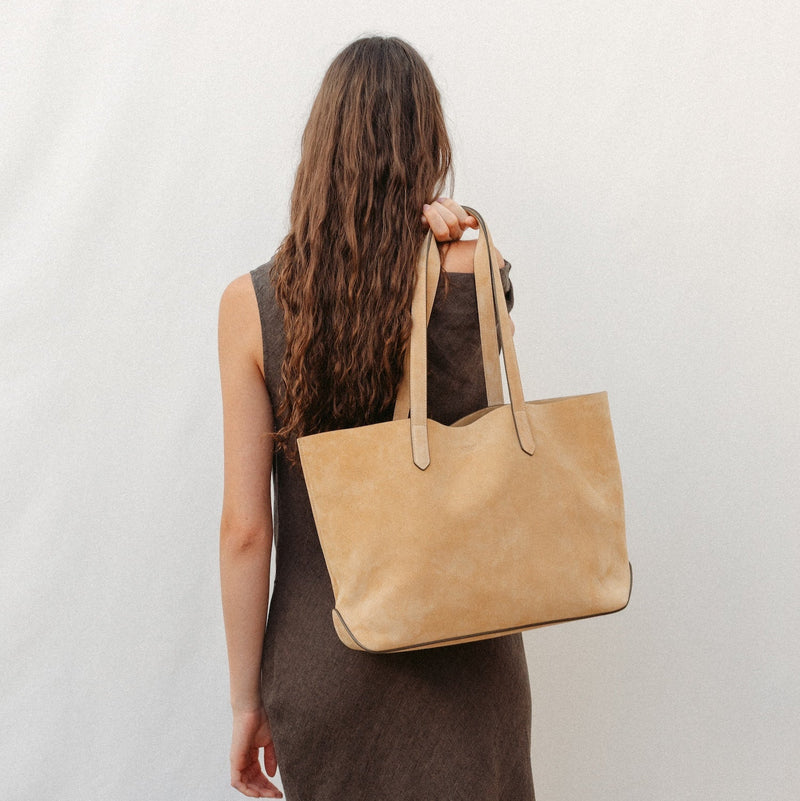 Model holding STOW London's summer Everyday Tote in Soft Sand Suede, featuring a small embossed STOW London on the front panel 