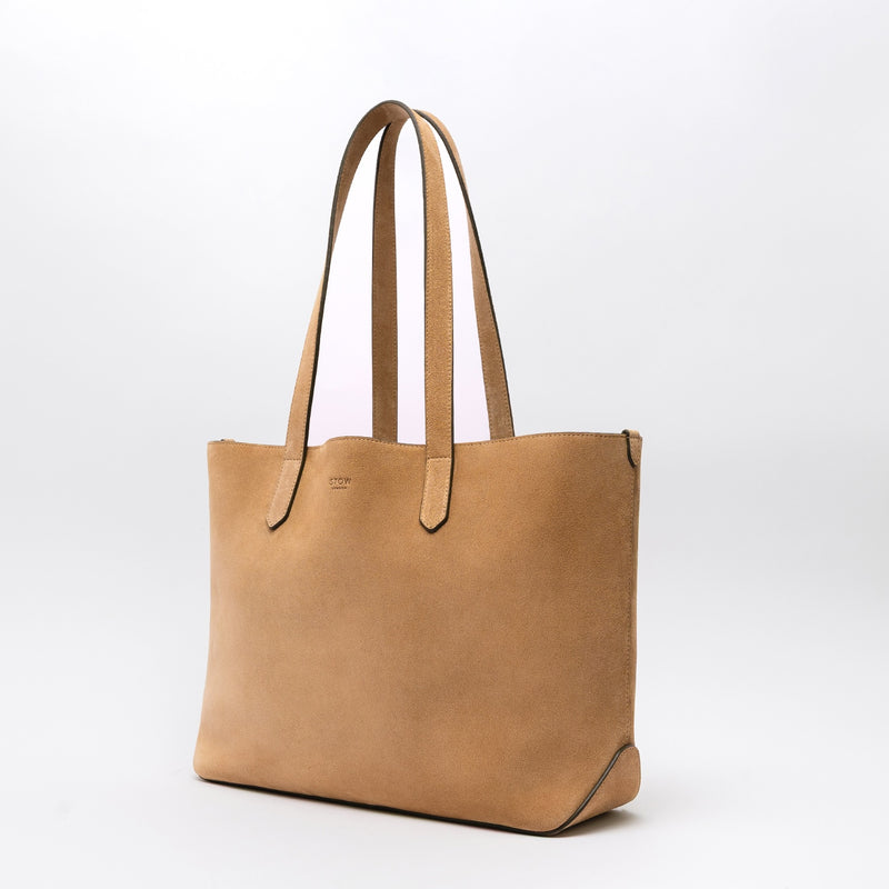 Off-axis view of STOW London's Everyday Tote bag in Soft Sand suede on a light grey background featuring a small STOW London logo embossed on the front panel 