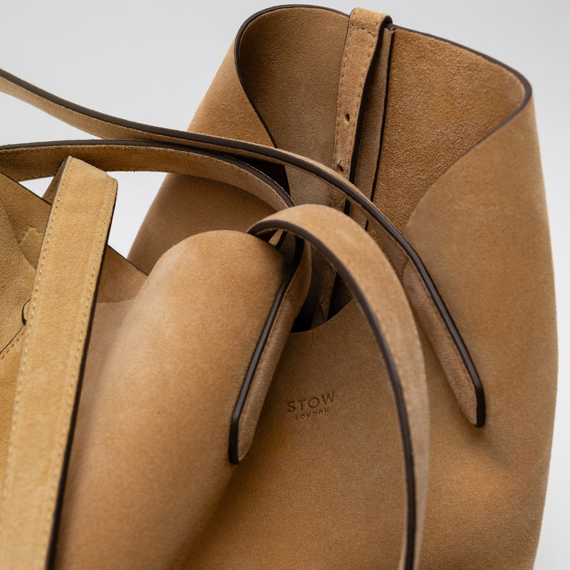 Close up of STOW London's Everyday Tote bag in Soft Sand suede on a light grey background featuring a small STOW London logo embossed on the front panel 