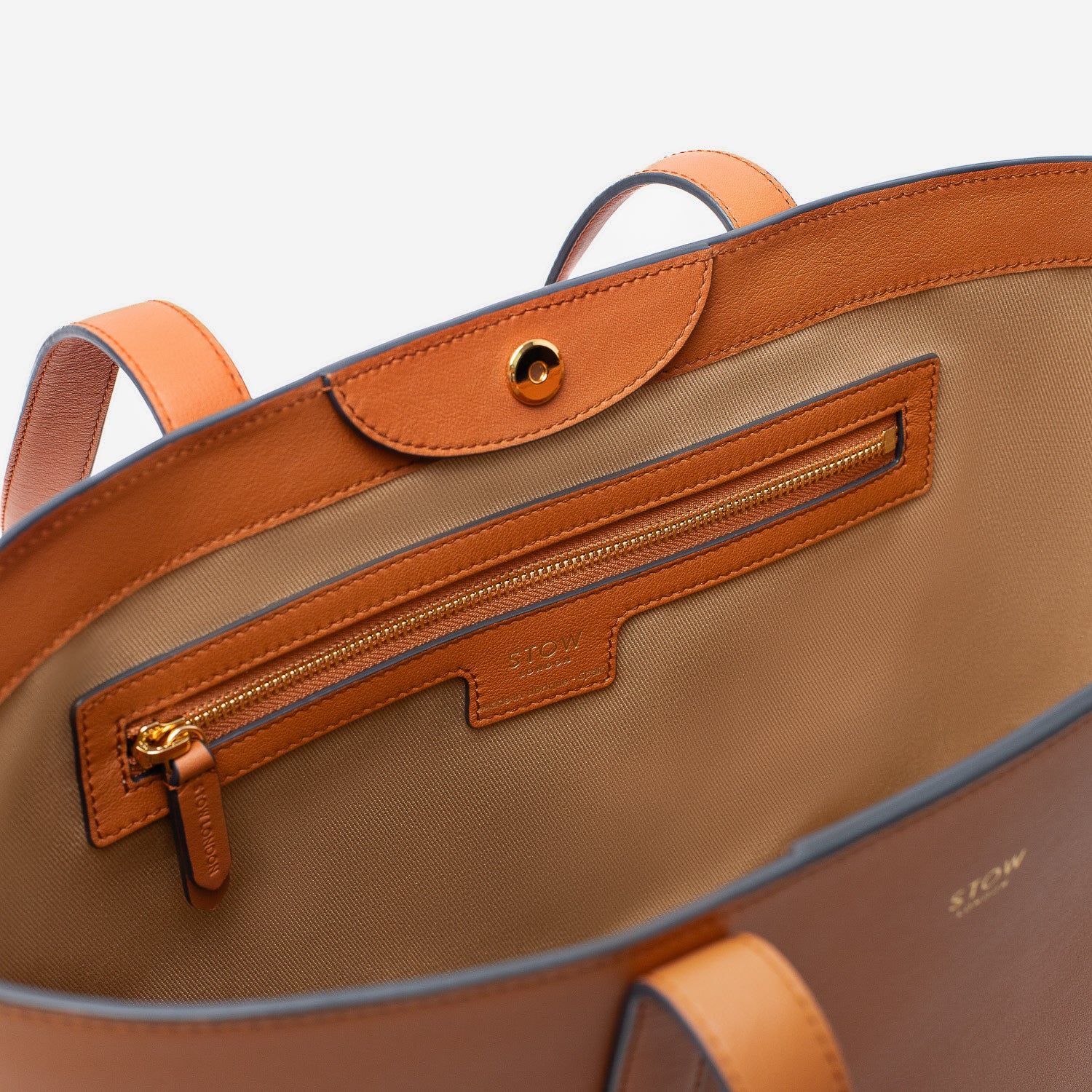 Close up of interior of Stow London's Everyday Tote Bag in Earth Tan smooth leather on a light grey background featuring the zip pocket and magnetic closure