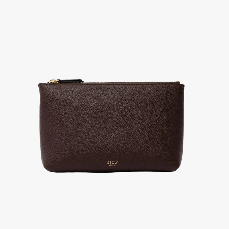 STOW London's travel pouch in Espresso pebbled leather on a light grey background featuring a YKK zip and a fine gold embossed logo on the front bottom 