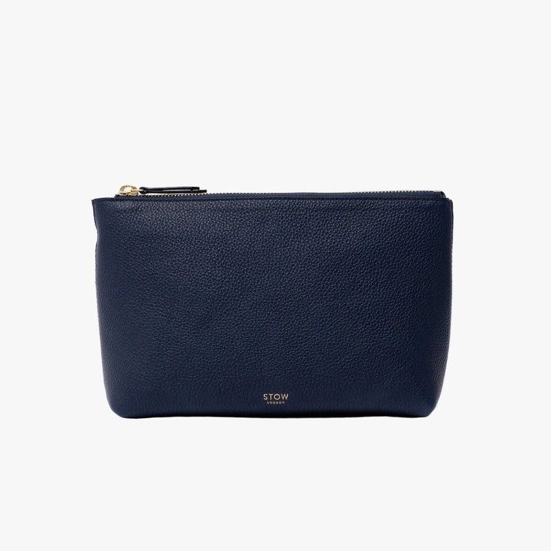 STOW London's travel pouch in Navy pebbled leather on a light grey background featuring a YKK zip and a fine gold embossed logo on the front bottom 