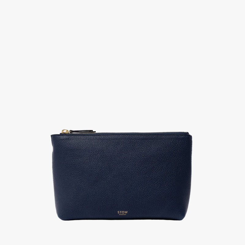 STOW London's travel pouch in Navy pebbled leather on a light grey background featuring a YKK zip and a fine gold embossed logo on the front bottom 
