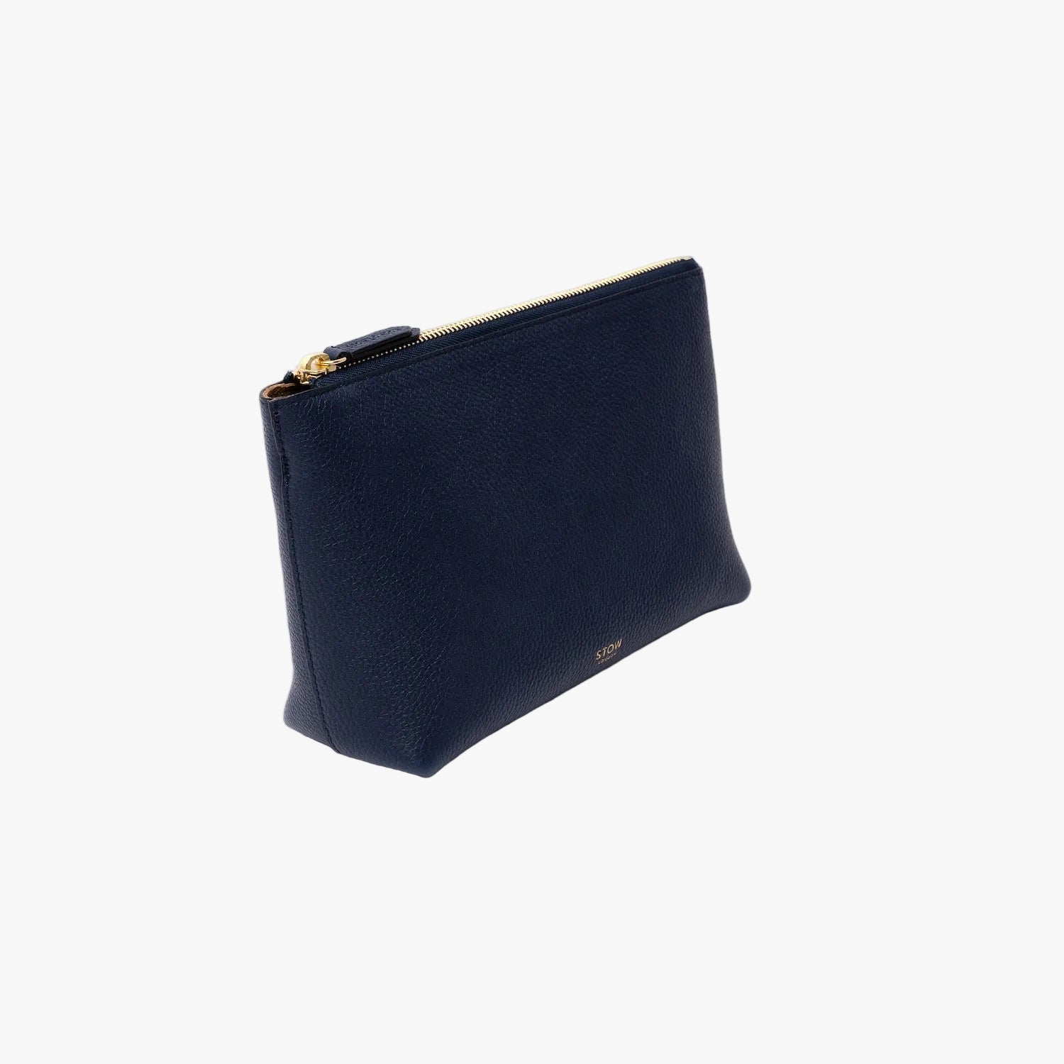 Off-axis view of STOW London's travel pouch in Navy pebbled leather on a light grey background featuring a YKK zip and a fine gold embossed logo on the front bottom 