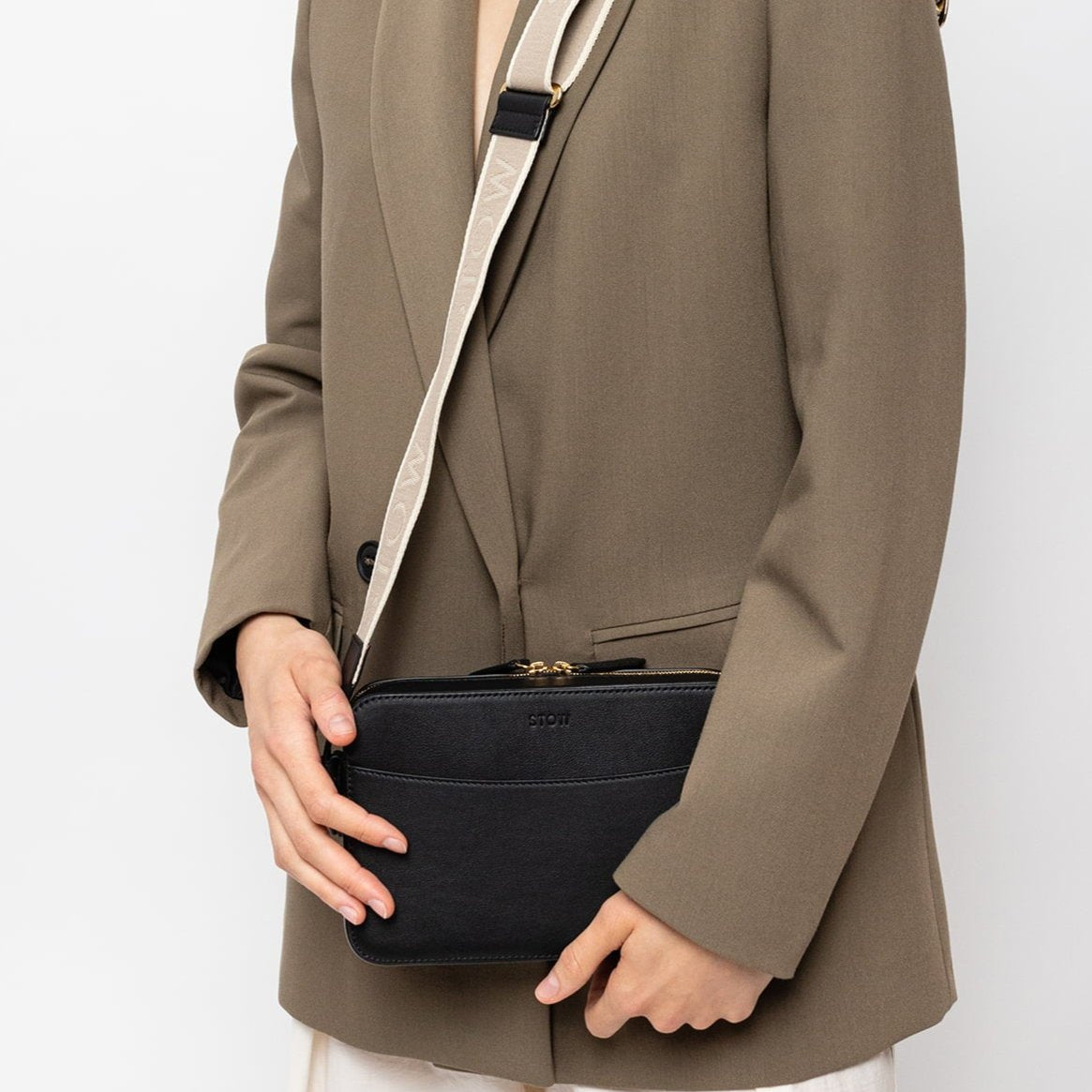 STOW London Camera Bag in Black leather with nastro strap. Worn by female model wearing taupe blazer and a baseball cap