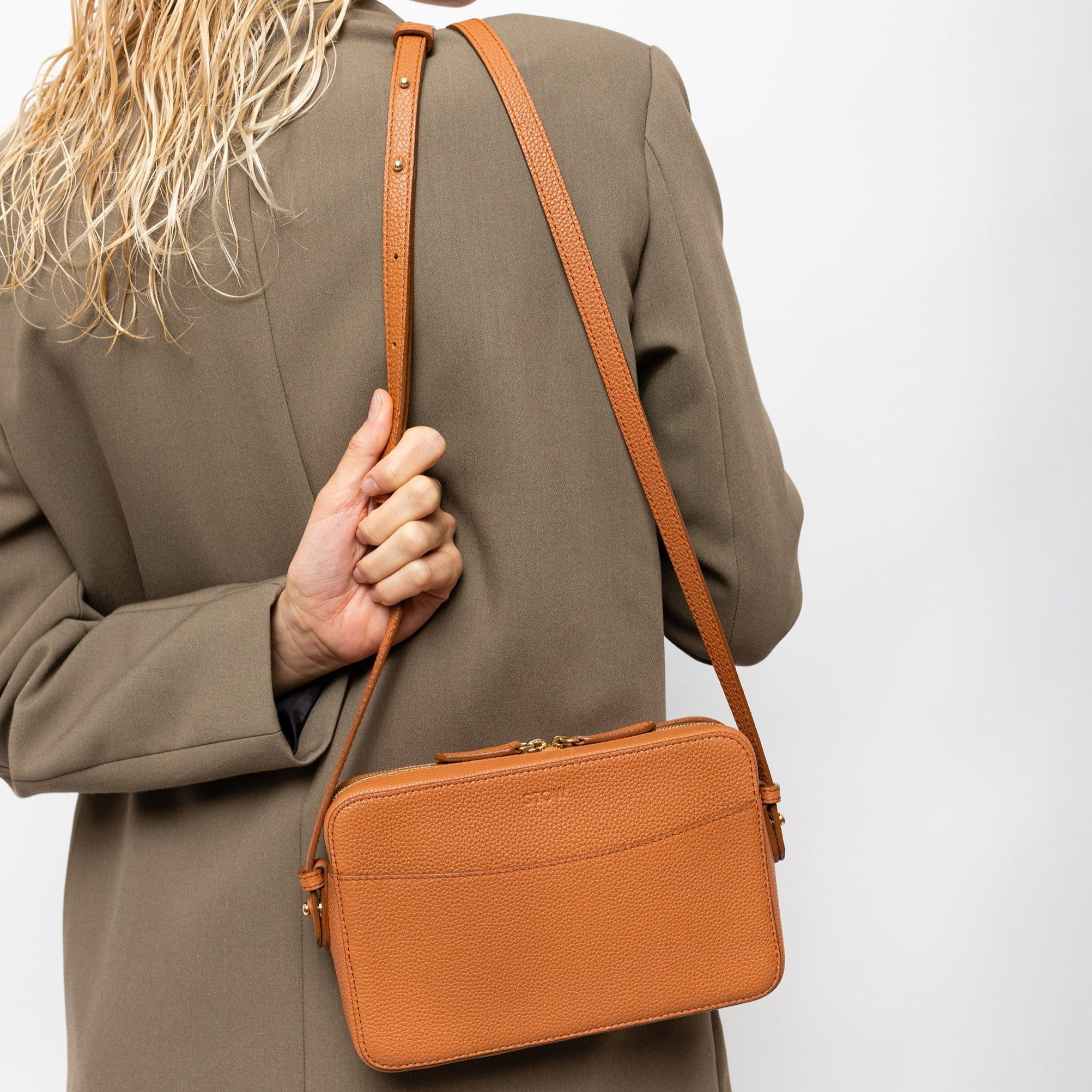 STOW London Camera Bag in Earth Tan leather, studio image of product carried by female model wearing taupe blazer