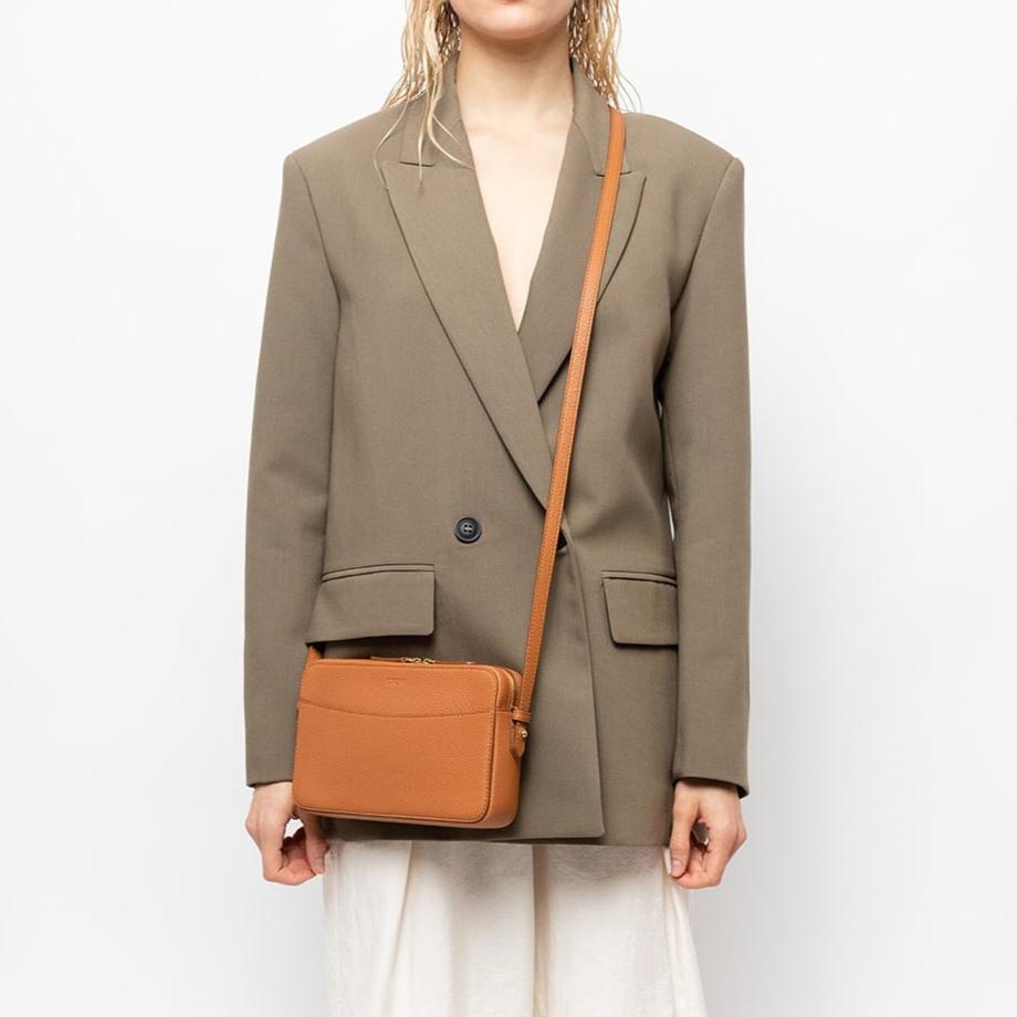 STOW London Camera Bag in Earth Tan leather, studio image of product carried by female model wearing taupe blazer