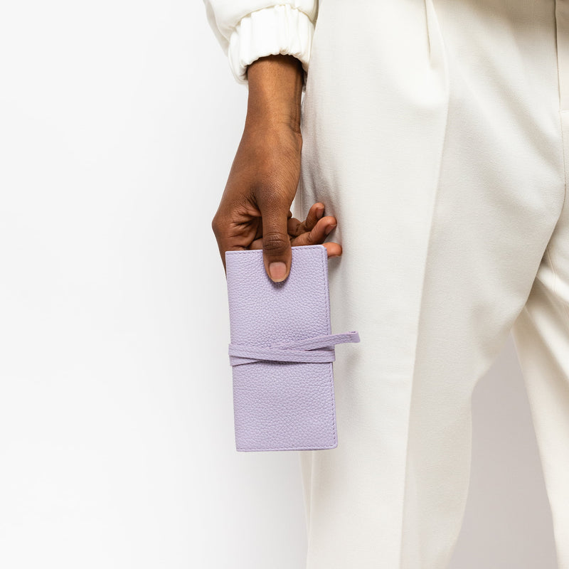 STOW London Mini Jewellery Roll in Wild Lavender leather, held by model wearing white suit in one hand