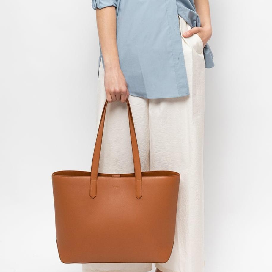 STOW London Earth Tan Leather Everyday Tote Bag, studio image with female model holding bag