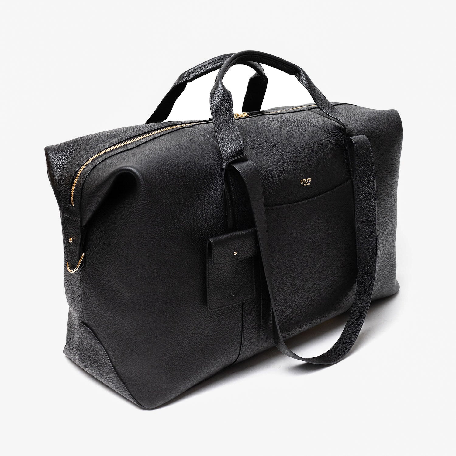Off-axis view of STOW London's Weekend bag in Black pebbled leather featuring detachable pouch and gold-coated stainless steel hardware on a light grey background