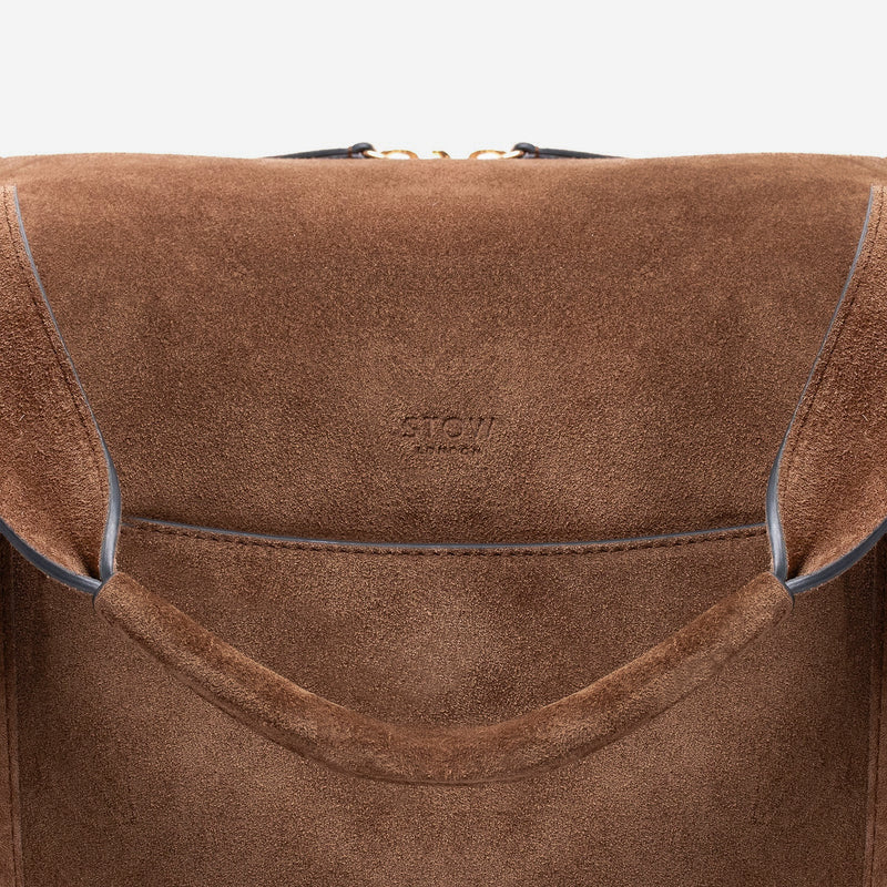 Close up shot of STOW London's Weekend bag in Chocolate suede leather featuring STOW London embossed logo on a light grey background