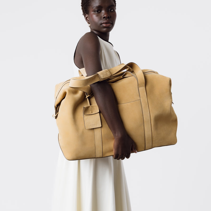 Model holding STOW London's Weekend bag in Soft Sand suede leather on a white background