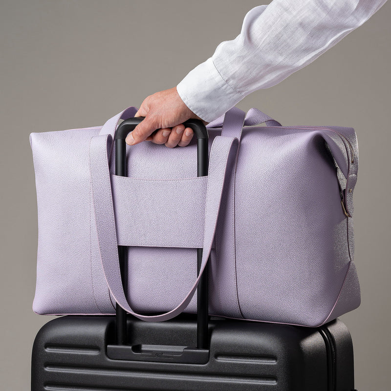 STOW Leather Weekend Bag in Wild Lavender pebbled leather being pulled on top of wheeled luggage by model.