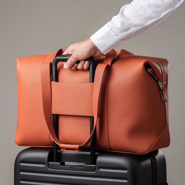 STOW Leather Weekend Bag in Clay Orange pebbled leather being pulled on top of wheeled luggage by model.