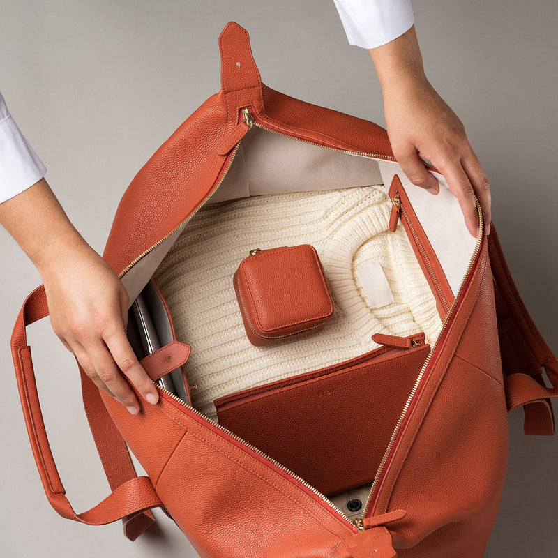 STOW Leather Weekend Bag in Clay Orange pebbled leather being opened by model showing contents inside.