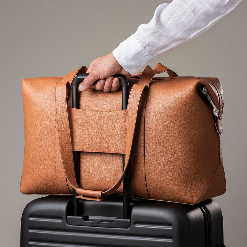 STOW Leather Weekend Bag in Earth Tan pebbled leather being pulled on top of wheeled luggage by model.
