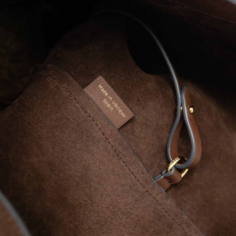 Close up of the interior of STOW London's Maxi Curve bag in Chocolate suede leather featuring gold-coated stainless steel d-ring on a light grey background