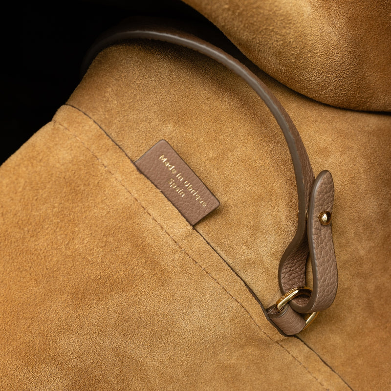 Close up of the suede interior of STOW London's Maxi Curve bag in Mocha pebbled leather featuring a gold-coated stainless steel d-ring on a light grey background