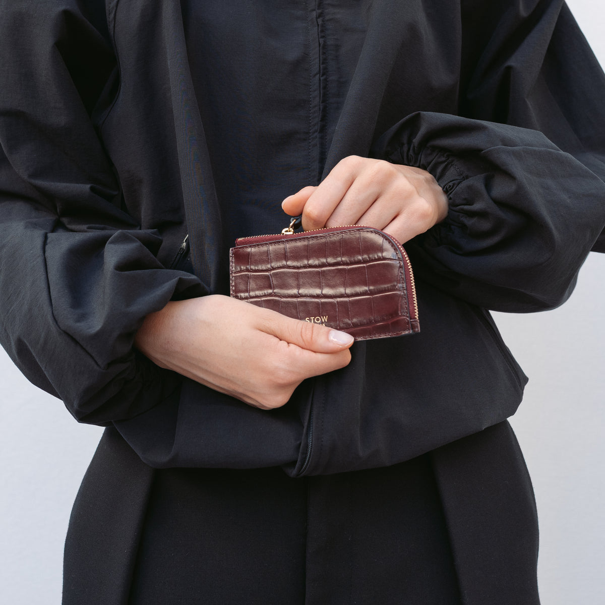 Model holding STOW London's Zip Wallet in Burgundy Embossed Croc leather featuring a small gold embossed logo on the front 