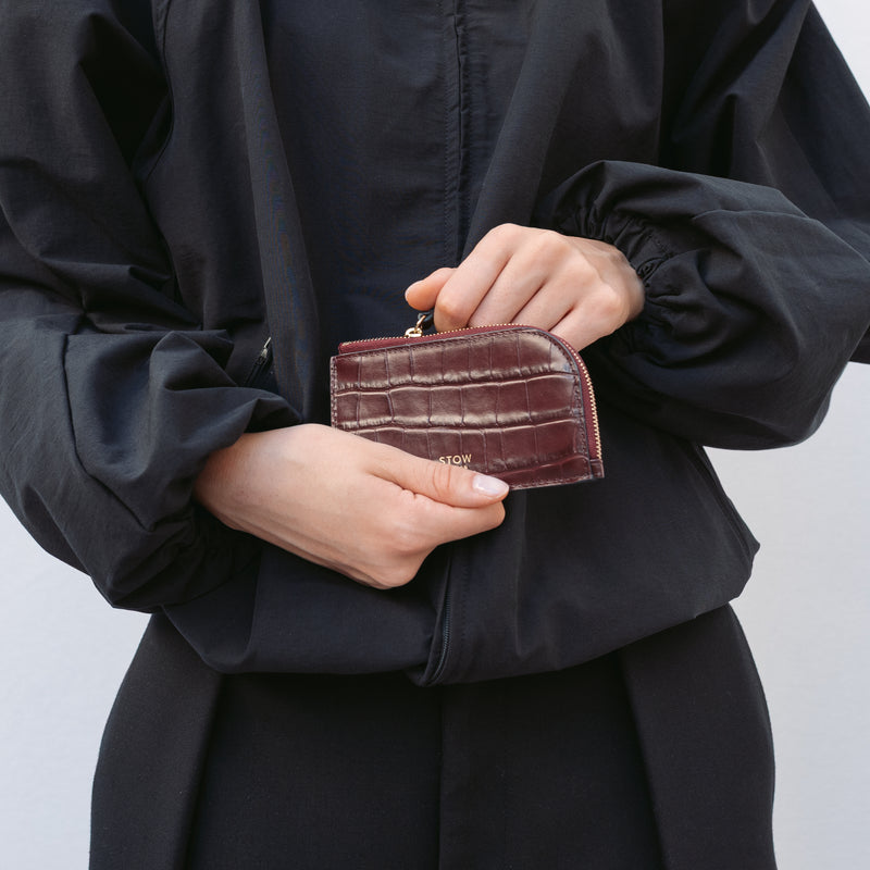 Model holding STOW London's Zip Wallet in Burgundy Embossed Croc leather featuring a small gold embossed logo on the front 