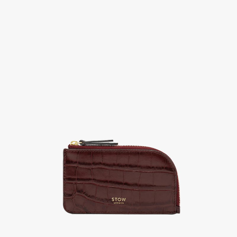 STOW London's Zip Wallet in Burgundy Embossed Croc leather on a light grey background featuring a fine gold embossed logo and YKK Natulon zipper