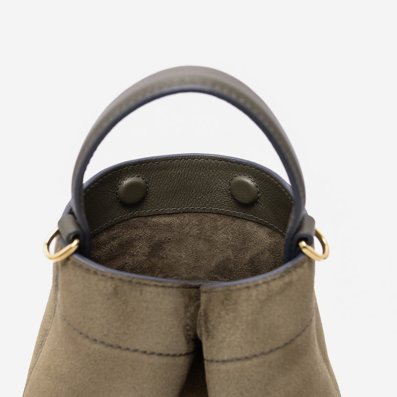 Close up of the top of Stow London's Mini Curve in Dark Green suede leather featuring hidden magnets and gold-coated stainless steel hardware on a light grey background 