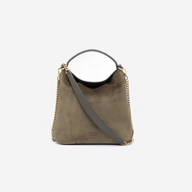 Stow London's Mini Curve in Dark Green suede leather and detachable chain strap styled as a flap bag featuring gold-coated stainless steel hardware on a light grey background 